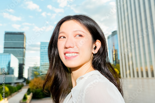 Smiling Gen Z Chinese woman with earbud in city