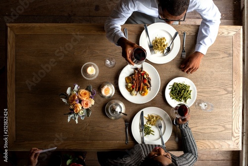 Top view of two people dining with wine and pasta on a wooden table.