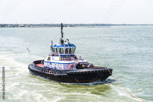 Foto Port tugboat escorting a merchant ship out to sea with a taut towing line attached, demonstrating safe ship handling in the navigation channel near Houston, Texas