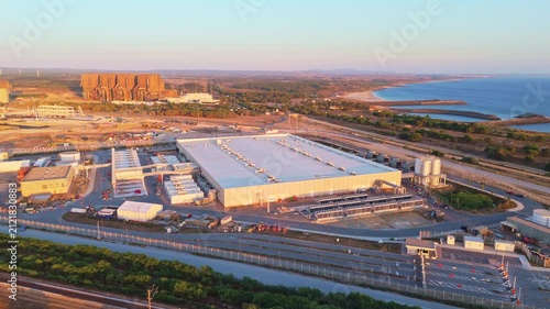 Data center building and expansion site under construction near the coastline in Portugal at sunset. Green landscape and Atlantic ocean. Aerial view. Moving upwards