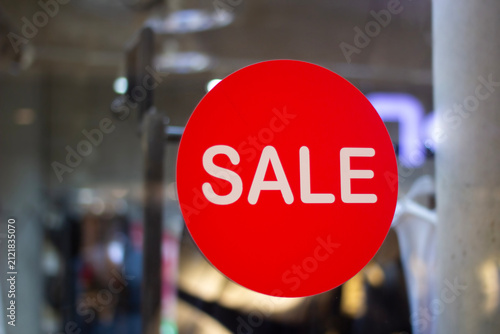 Horizontal photo. Red round sticker with text Sale on glass window, door of clothing store with mannequin. Concept of Black Friday, 11 november, , retail, 50% off, online shopping, cyber monday, gift