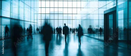 Blurred figures of people walking in a modern office building with large glass windows and a bright, cool-toned interior. The motion blur suggests movement and a bustling atmosphere