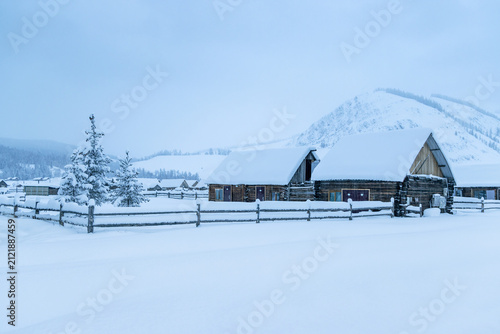 Obraz na płótnie A quiet winter rural scene featuring snow-blanketed wooden houses and a fence in a mountain village
