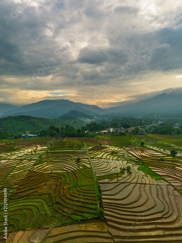 Aerial view of Sapa rice terraces at sunrise with golden light over green fields and misty mountain valleys