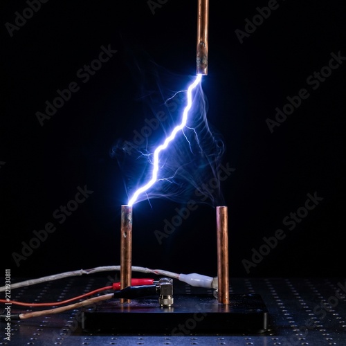 Bright blue plasma arc discharge between two metal electrodes against a dark background.