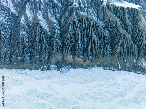 Fotografía A steep eroded mountain slope meets a frozen glacial ice field, showing geological landforms in cold regions