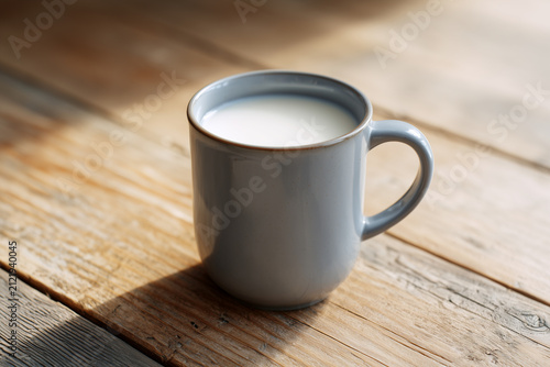 Fresh Milk in Grey Ceramic Mug on Rustic Wooden Table with Sunlight