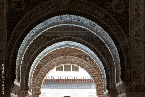 intricate Moorish architecture and horseshoe arches adorned with elaborate stucco work inside the Nasrid Palaces at the Alhambra in Granada, Spain.
