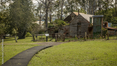 A path leads to the gate of an historic weathered timber cottage and shed in the foreground, close to an ex-whaling station of the past in Beowa national park near Eden in New South Wales, Australia. 
