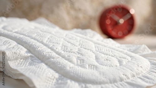 Close up of a sanitary pad with a red alarm clock in the background.