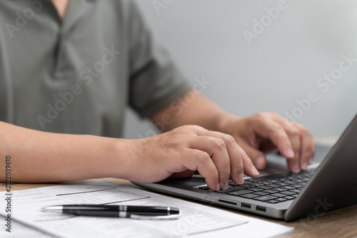 Businessman Typing Insurance Documents on Laptop with Paperwork on Office Desk, Digital Data Entry, Online Insurance Checklist, Policy Processing, Documentation Management and Business Administration