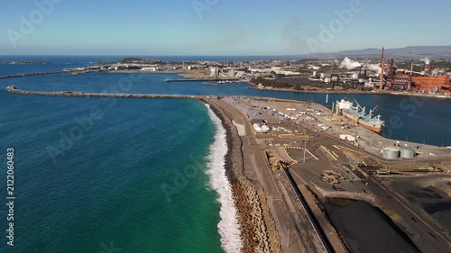 Aerial drone view of Port Kembla, Illawarra Region, NSW, Australia showing visible plumes rising from industrial chimneys, the seaport, industrial complex and small harbour foreshore in August 2026   