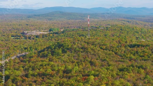 AERIAL: Telecommunications tower rises from expansive forest displaying early autumn colours near Otočac, Croatia. Contrasts between modern communication infrastructure and colourful rolling landscape