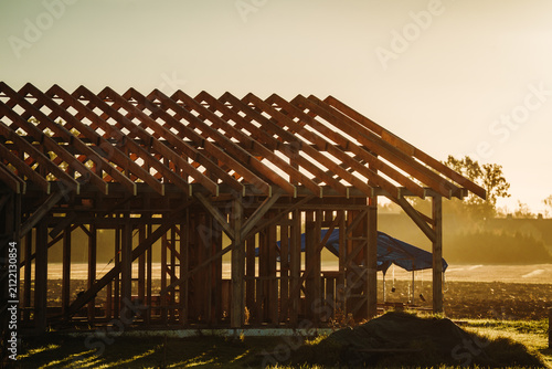 Close-up of timber roof trusses and wooden framing during residential house construction in warm golden-hour light.