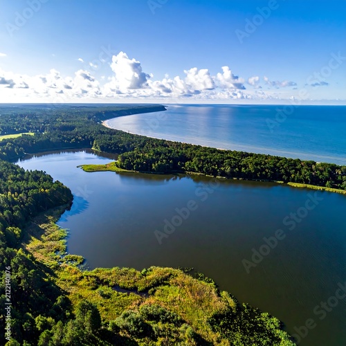 Scenic Coastal Lagoon and Forested Shoreline Curving Along Blue Sea Under Cloudy Sky