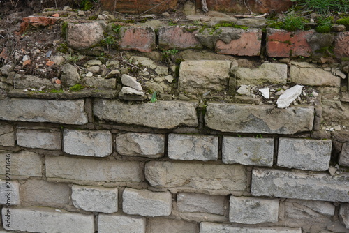 A light gray wall, an old building, a fence with green moss and moisture. Light gray, red bricks, beautiful, stylish brickwork.