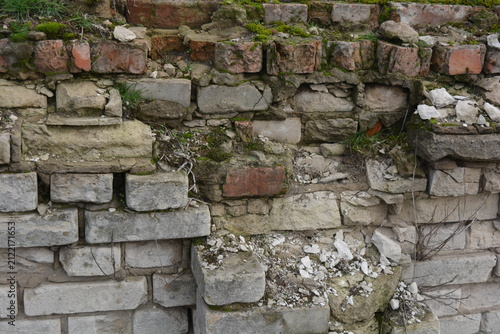 A light gray wall, an old building, a fence with green moss and moisture. Light gray, red bricks, beautiful, stylish brickwork.