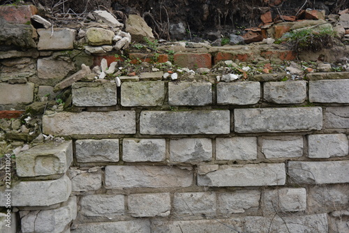 A light gray wall, an old building, a fence with green moss and moisture. Light gray, red bricks, beautiful, stylish brickwork.