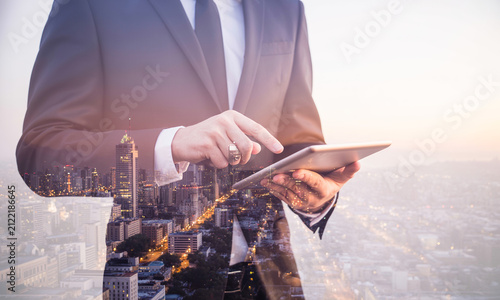 Double exposure of businessman touching digital tablet screen against city skyline background.