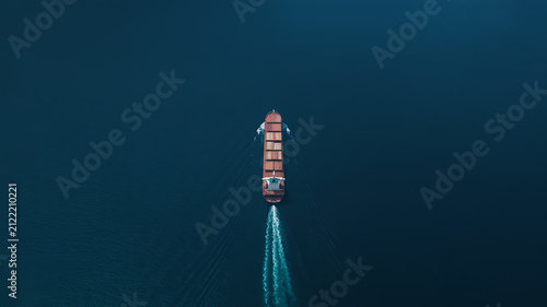 Large container ship sailing on deep blue ocean water seen from high angle aerial view showing cargo transportation and global logistics movement across the sea during a calm day journey