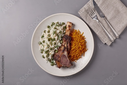 Baghali Polo plated with grilled pork chop, fluffy mashed potatoes, bright green peas, dill, shredded cheese. Concept of rice with dill broad beans lamb meal presentation.