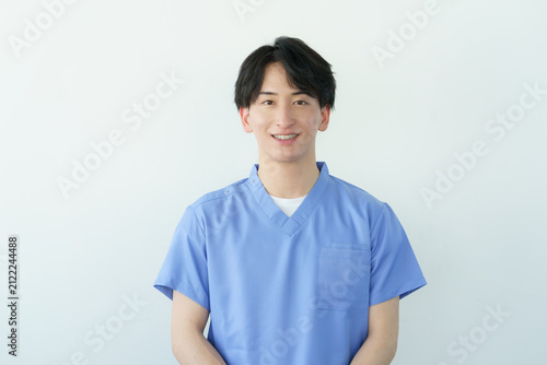 白背景のスクラブを着た若い日本人男性整体師