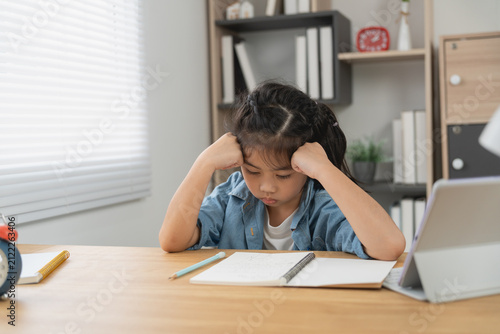 Canvas Print Young girl sitting at wooden desk with notebook and pencil frustrated struggling