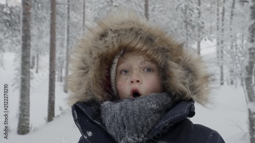Young girl with fur hood and scarf standing in snowy forest as visible breath steams from her mouth in the cold winter air