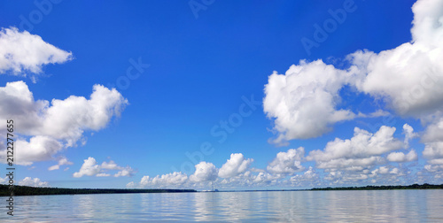 Photography Serene lake with calm water and white clouds on blue sky