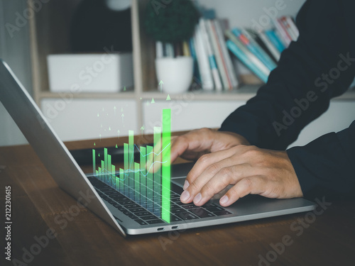 Laptop computer with business graph on screen, hands typing on keyboard in office interior, data analysis and finance concept, focused work