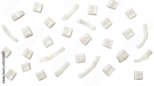 Close-up top view of various white coconut pieces, including diced squares and curved strips, scattered on a clean white background.