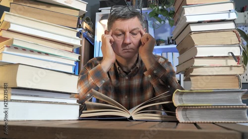 Mature Man Studying Among Stacks of Books in Cozy Home Library Room, quiet academic environment showing dedication, scholarship, personal growth and intellectual curiosity