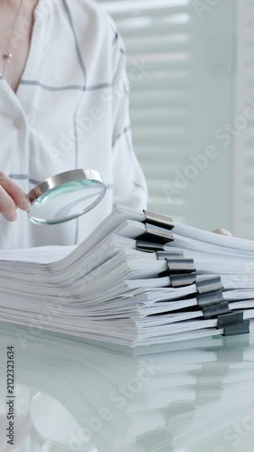Woman's hands using a magnifying glass to scrutinize a document while holding a pen, researching important information for legal, financial, or academic analysis and validation