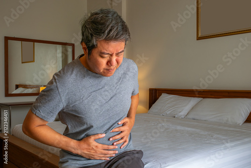 Person holding stomach in pain, illustrating abdominal disorders and medical treatment concept in home setting.