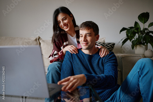 Couple Using Laptop Together at Home. Boyfriend and Girlfriend Sitting on Couch in Cozy Apartment Using Computer.