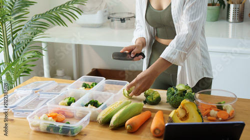 Woman cutting fresh broccoli while preparing healthy vegetable meals in reusable food containers at home. Nutrition and healthy lifestyle concept.