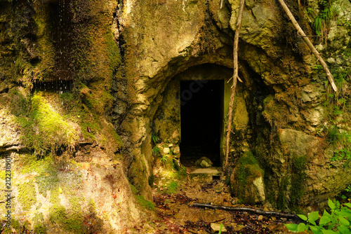 Foto Dark tunnel opening carved into a mossy rock cliff face near Idrijca River and Divje Jezero lake in Slovenia