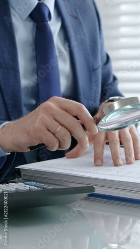 Professional financial auditor investigating corporate documents and reports with a magnifying glass. Analyzing numbers and text for accuracy. Conducting research