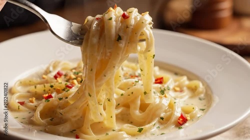 Close-up of a fork twirling creamy pasta with chili flakes and fresh herbs.