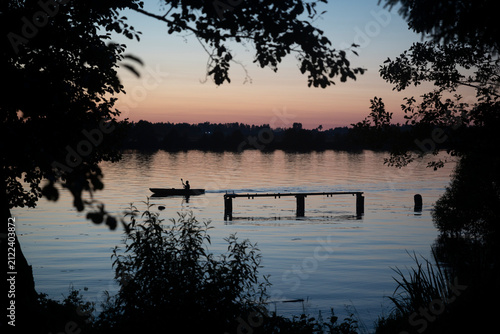 Silhouette of person kayaking on calm lake at sunset with wooden pier