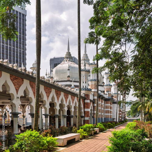 View of the historic Jamek Mosque featuring iconic Moorish architecture, white domes, and arched walkways surrounded by palm trees in the city center in Kuala Lumpur, Malaysia