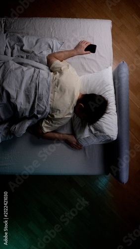 Obraz na płótnie Person sleeping on a bed at night, still holding a mobile device after prolonged