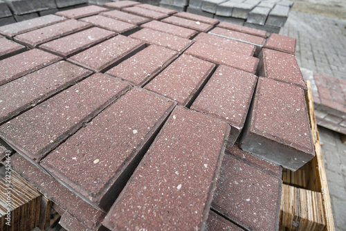 Red pavers are neatly arranged and stacked on a wooden pallet at a construction site. Materials are ready for upcoming projects during the day