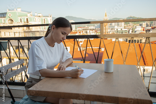 Canvas Print young traveler takes handwritten notes on a sunny rental terrace, blending acade