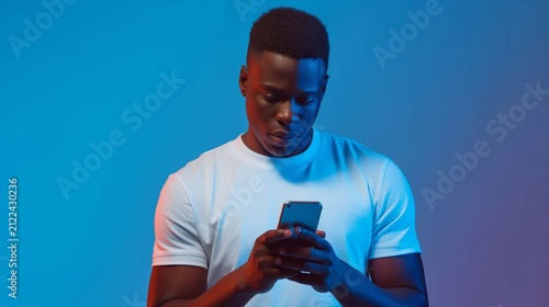 A man at his smartphone with a focused expression, standing in front of a solid blue background