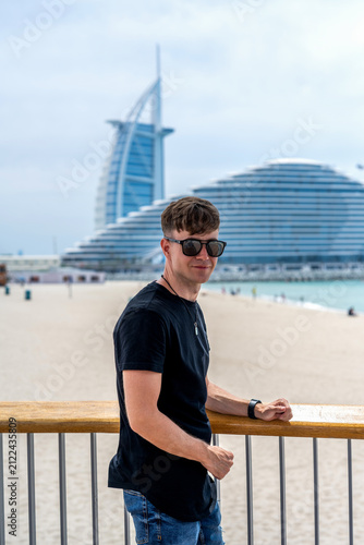Obraz na plátně Young man smiling at camera on boardwalk with Dubai landmark view