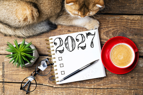 New year resolutions 2027 on desk. 2027 resolutions list with notebook, coffee cup, cute cat on table. Goals, resolutions, plan, cozy, hygge concept. New Year 2027 template, copy space