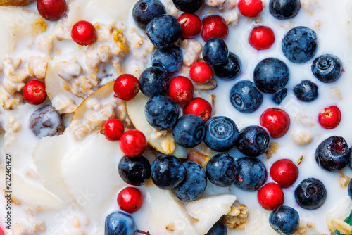 Overhead closeup of muesli with milk, oats, sliced pear, wild bilberries and red lingonberries. 
