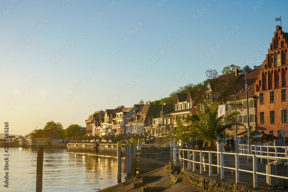 Obraz premium Golden Hour along Meersburg Promenade with Historic Waterfront and Palm Trees on Lake Constance