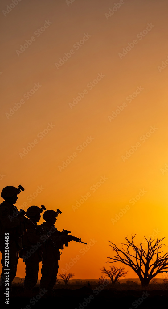 Obraz premium Silhouettes of soldiers with rifles stand in a desert landscape at sunset, symbolizing strength, vigilance, and resilience against a warm, vibrant sky